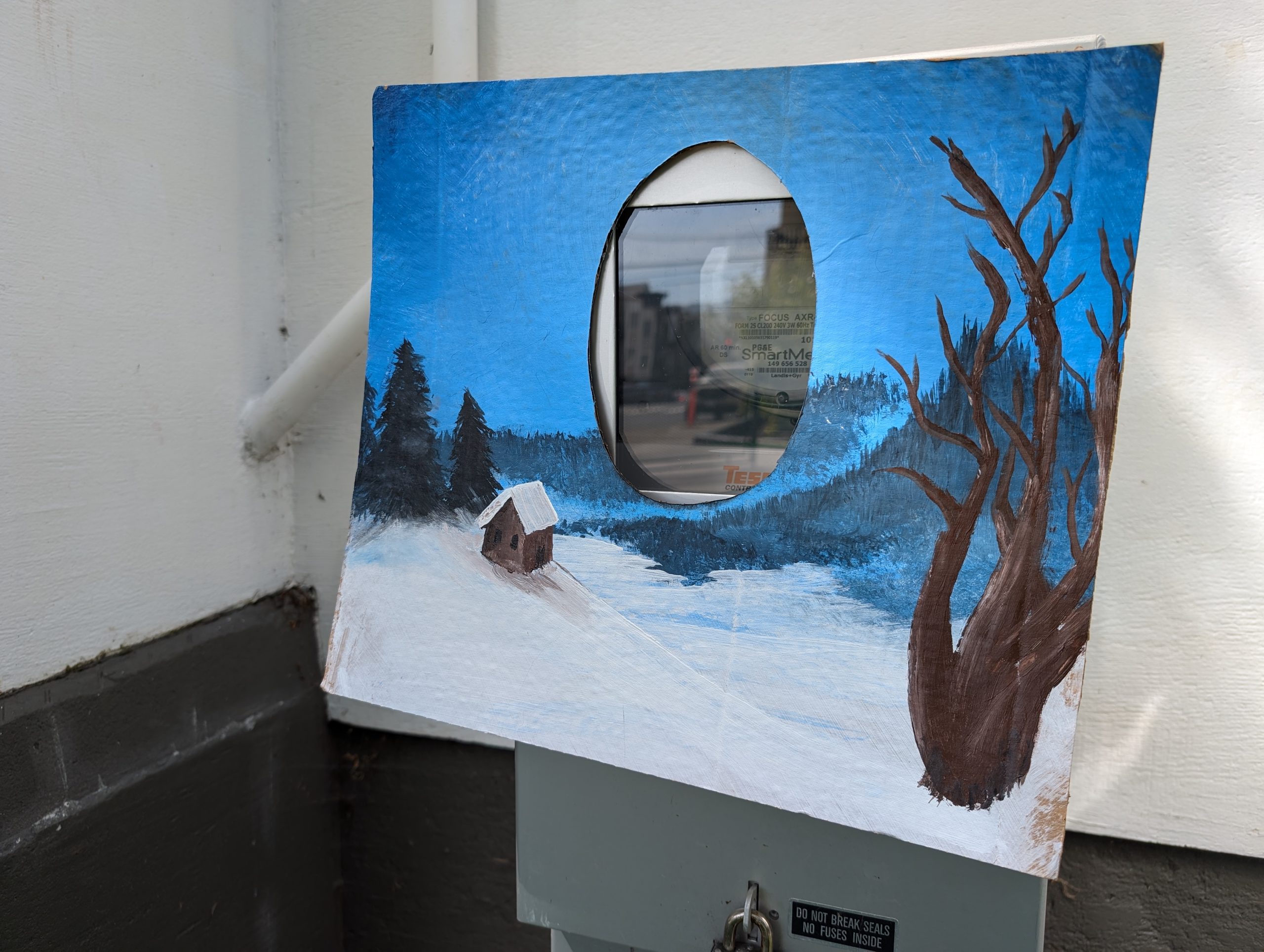 Hand-painted winter landscape on a canvas with a circular cutout in the middle, revealing a urban utility box mounted on the wall with street scene reflected on the box.