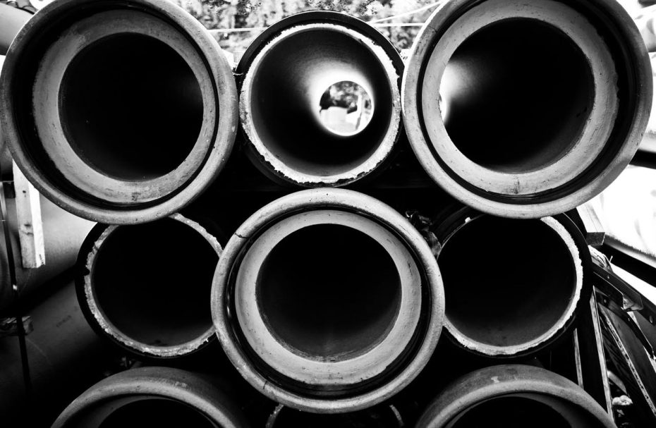 Black and white photo of a stack of large industrial pipes, viewed from one end, showing the circular openings.