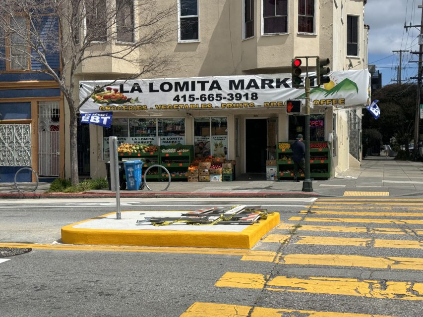 A street corner view of la lomita market with colorful grocery display and yellow pedestrian crosswalk in front.
