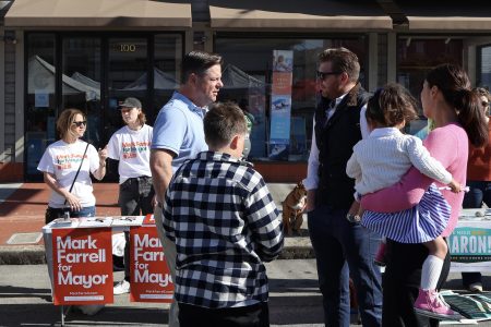 A man interacting with a group of people, including children, at an outdoor campaign booth for "mark farrell for mayor.