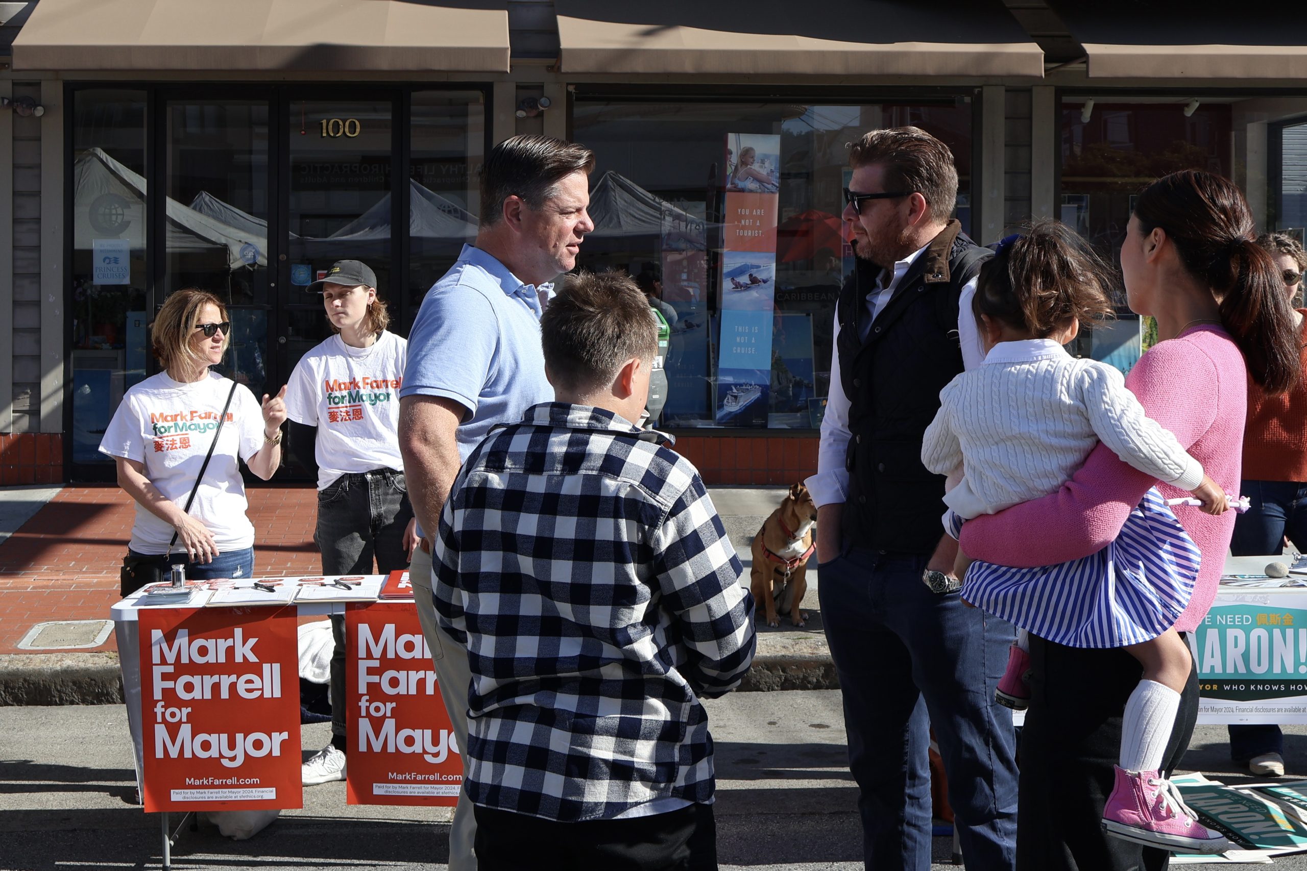 A man interacting with a group of people, including children, at an outdoor campaign booth for "mark farrell for mayor.