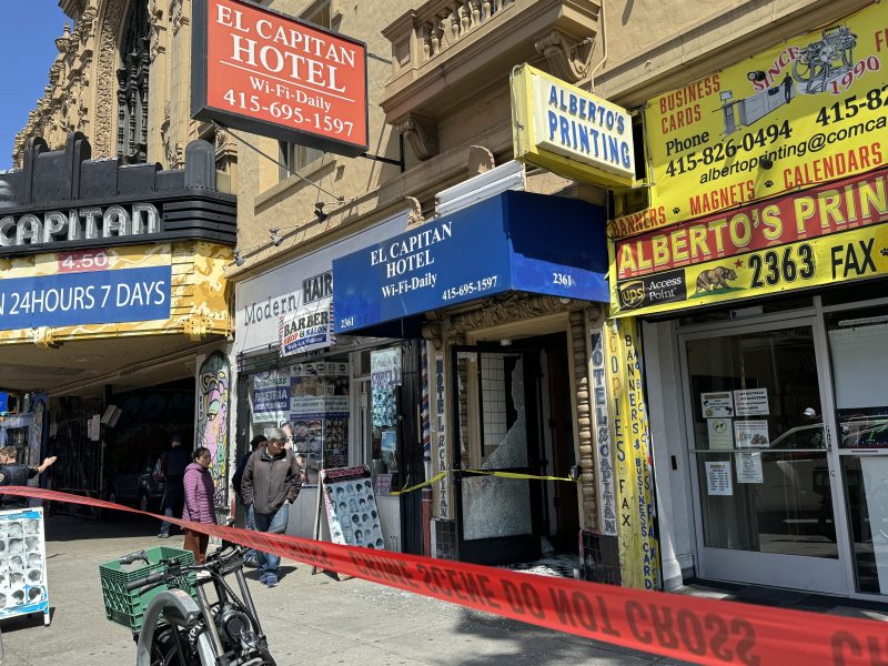 Storefronts with caution tape across the foreground on a sunny day.
