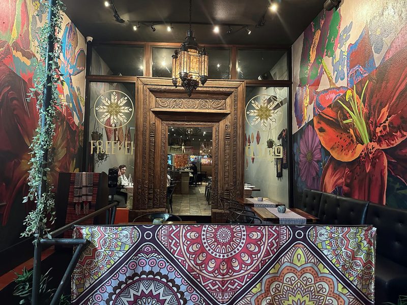 Elegant restaurant interior with vibrant floral murals and ornate wooden door.