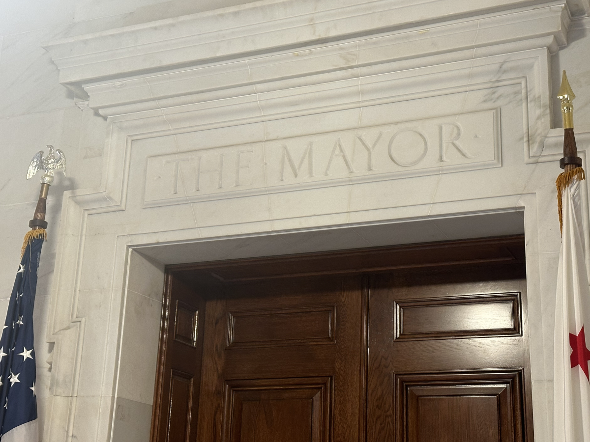 Engraving in marble reading "the mayor" above a wooden door flanked by two flag poles