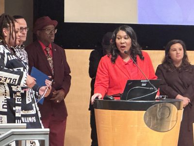 London Breed standing at a podium surrounded by people