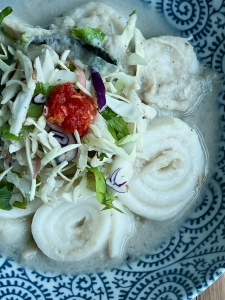 A bowl of traditional noodle soup with sliced fish cakes, shredded cabbage, and a dollop of red chili paste.