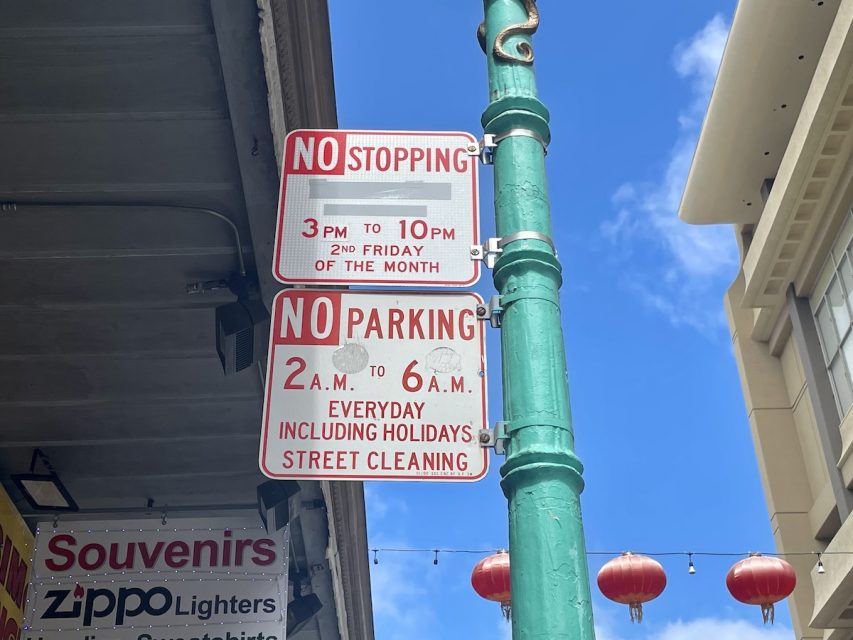 Two traffic signs on a pole indicate no stopping 3 pm to 10 pm on the second Friday of the month and no parking 2 am to 6 am daily for street cleaning,