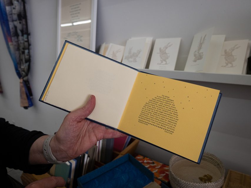 A person holds a book open to a page with text formed in a beehive shape