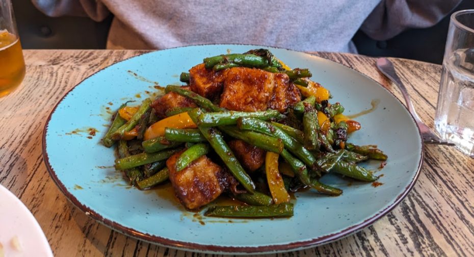 A plate of stir-fried chicken with green beans and bell peppers served on a blue dish, placed on a wooden table.