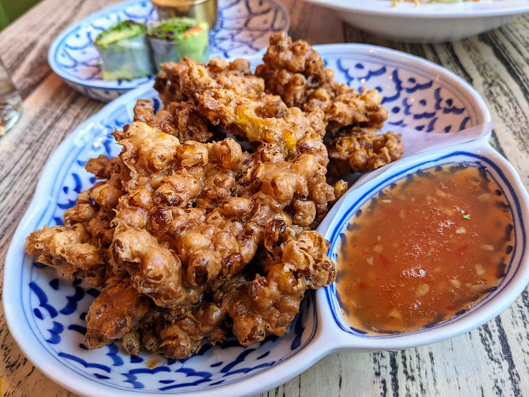 A plate of crispy fried squid served with a side of spicy sauce and a small dish of cucumbers.
