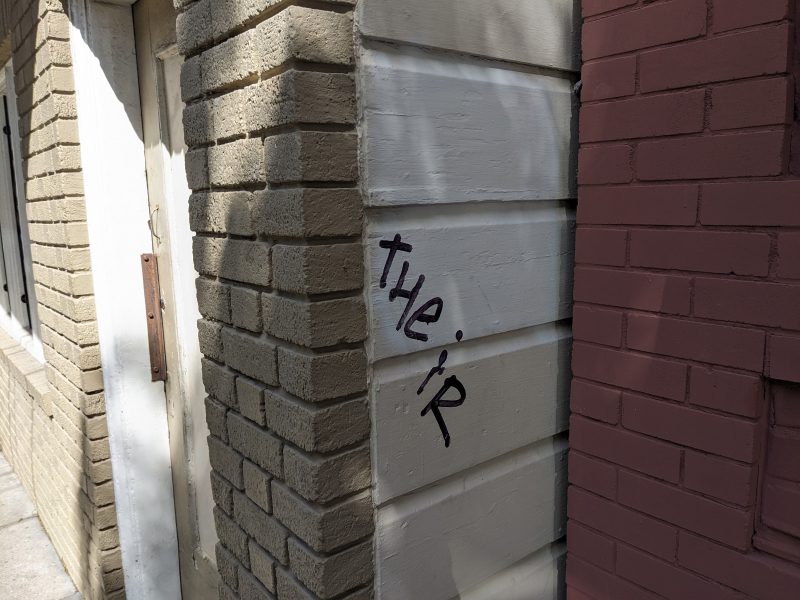 The word "their" spray-painted on a corner of a building with contrasting brick colors.