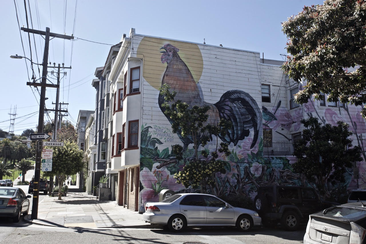 Urban street with a large mural of a rooster on a building's side wall.