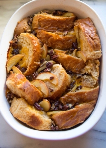 A rectangular baking dish containing bread pudding with sliced apples and pecans.