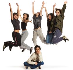Five young adults are jumping joyfully with their arms raised against a white background, while one person sits on the floor looking up at them.