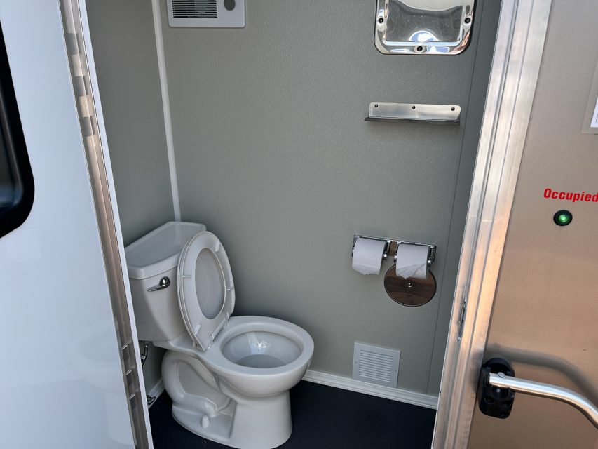 Interior of a clean lavatory with an unoccupied sign, showing a toilet, toilet paper holder, and metal handrails.