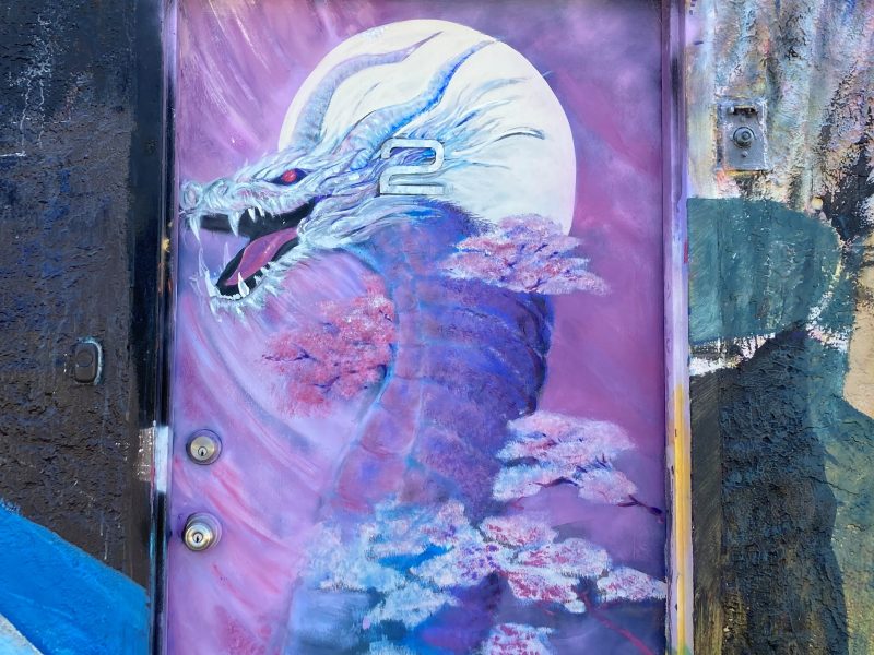 A vibrant mural of a dragon painted on an urban door, with the creature set against a moonlit sky and surrounded by pink clouds.