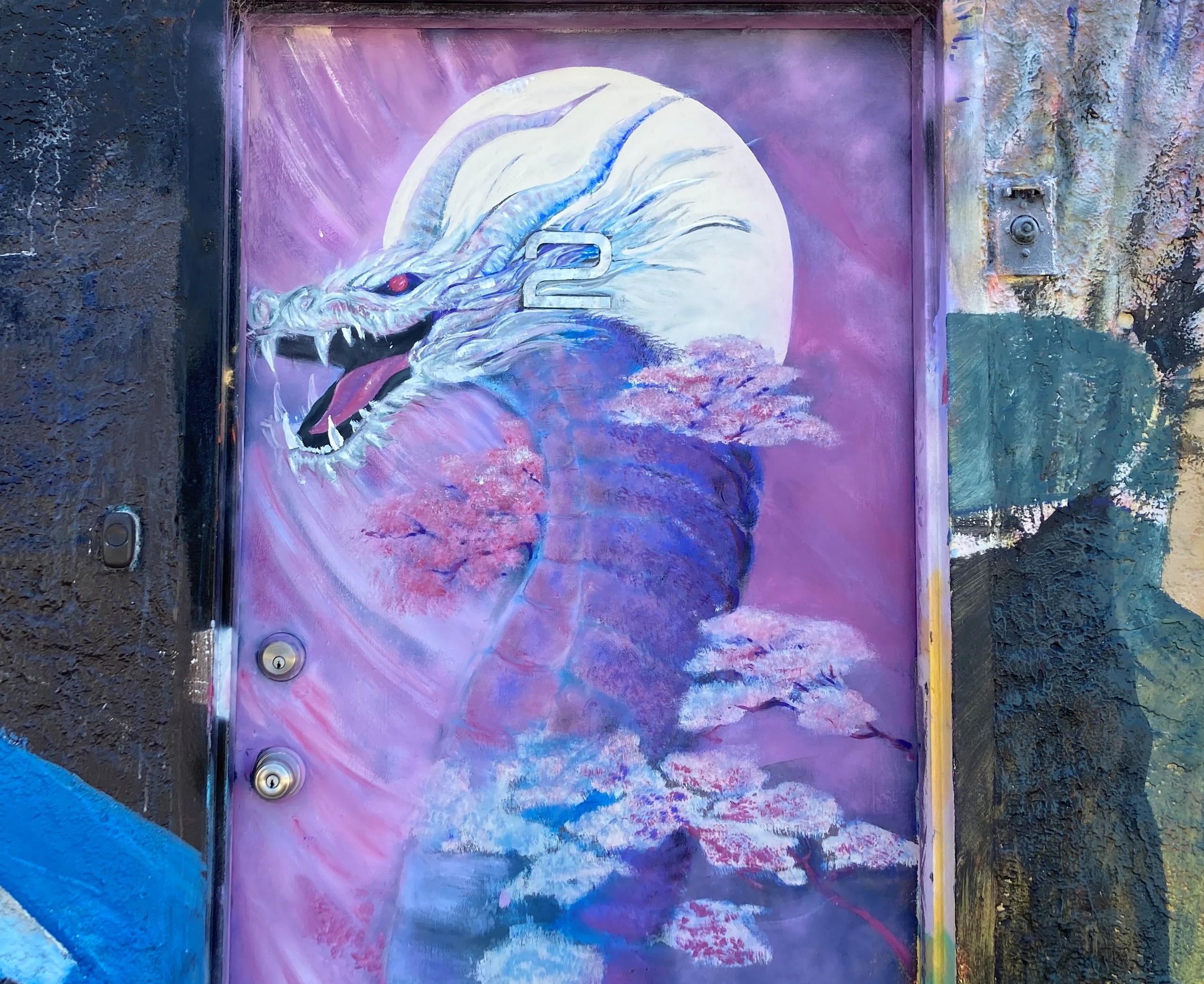 A vibrant mural of a dragon painted on an urban door, with the creature set against a moonlit sky and surrounded by pink clouds.