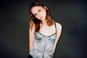 A young woman in a blue corset top posing against a dark background.