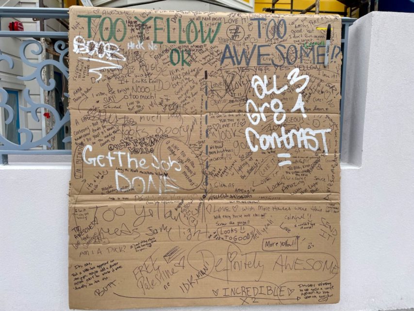 A large cardboard sign covered in handwritten messages and comments in various colors. Some phrases are written in large letters, like "Get the job done" and "Too yellow".