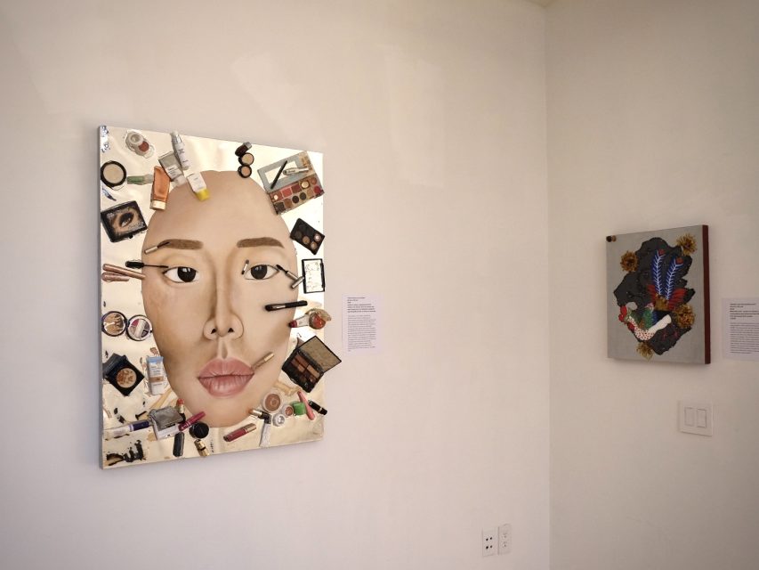 Art installation featuring two portraits made from cosmetics on a white wall. The left piece depicts a face surrounded by beauty products, while the right piece shows textured materials creating a face.