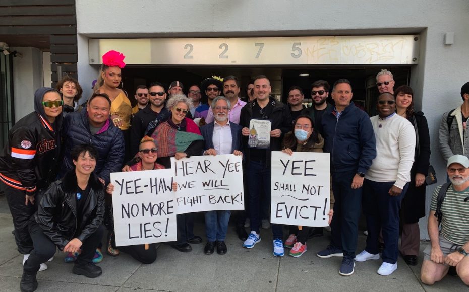 A group of people standing in front of a building, holding signs that read, "YEE-HAW HEAR YEE NO MORE LIES!", "HEAR YEE WE WILL FIGHT BACK!", and "YEE SHALL NOT EVICT!.