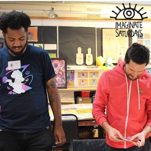 Two men engaged in a creative activity at a crafting table inside a room decorated with colorful artwork and "imagínate saturdays" banner.