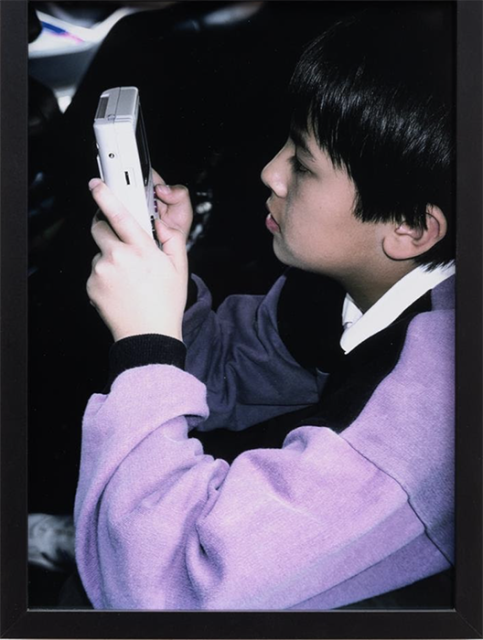 A young boy in a purple sweatshirt holds and looks intently at a portable gaming device.