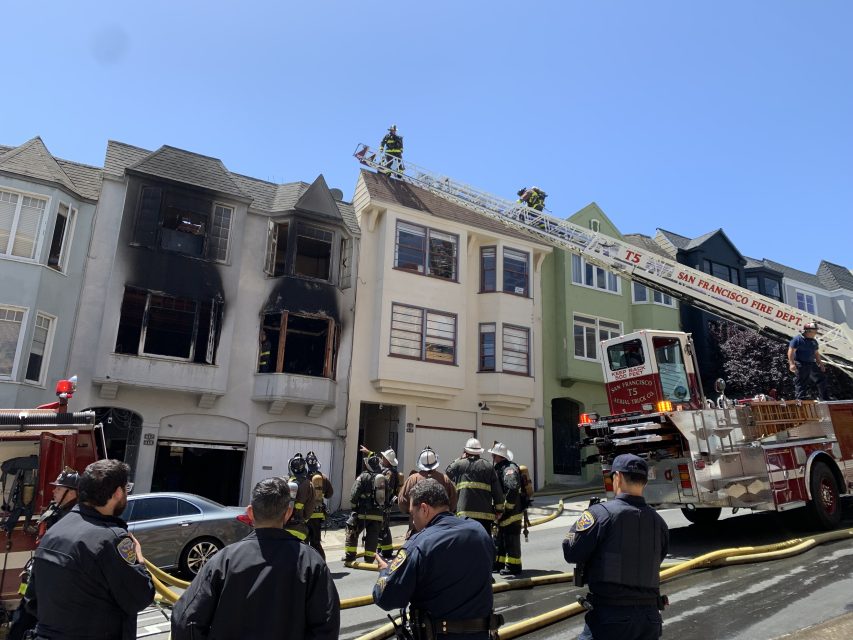 Firefighters and police at dog walker Terry Williams' home, with significant damage to a multi-story building. A fire truck ladder extends to the roof as firefighters assess and manage the situation.