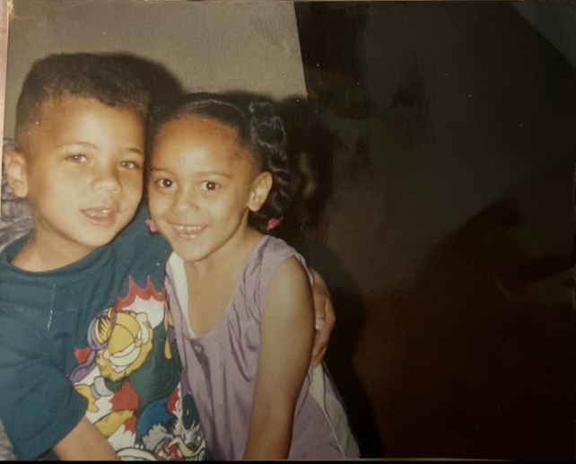 A young boy in a green Power Rangers shirt and a girl in a purple dress smile while hugging each other.