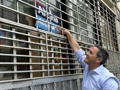 A person in a blue shirt is placing a blue and white sign behind the bars of a window on an old building.