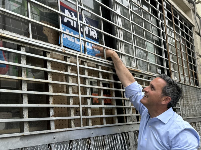 A person in a blue shirt is placing a blue and white sign behind the bars of a window on an old building.