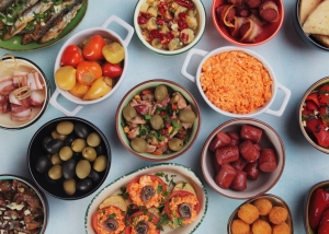 Assorted mediterranean dishes including olives, grilled fish, and various salads displayed in colorful bowls on a table.