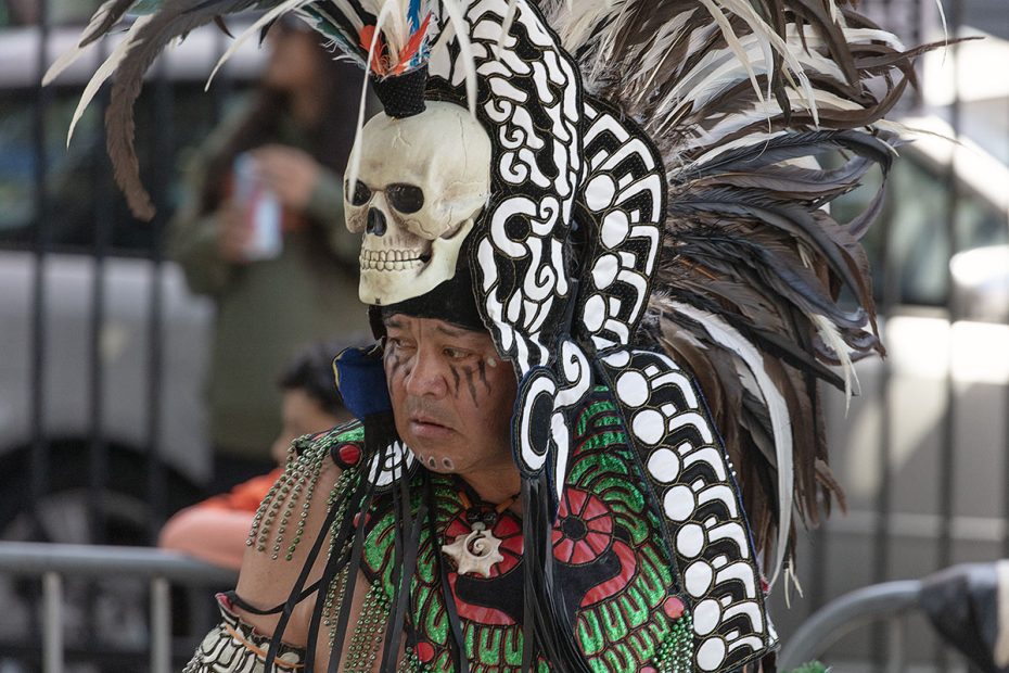 A person wearing an elaborate headdress made of feathers and a skull decorates their head while participating in a cultural event.