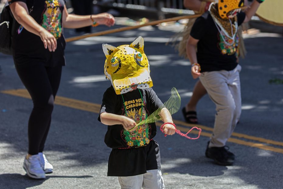 Children wearing colorful costumes and animal masks march in a street parade.