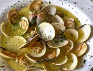 A plate of steamed clams in a garlic butter sauce, garnished with chopped parsley.