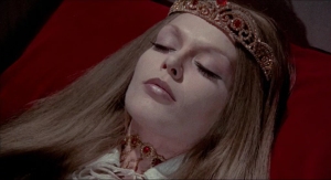 A woman wearing a crown and medieval attire lies with closed eyes, resembling a peaceful, royal figure in repose on a red background.