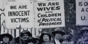 Women holding signs in a protest; one sign reads "We are innocent victims," and another reads "We are wives and children of political prisoners.
