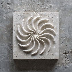 A square, white stone sculpture with a concentric, spiral pattern, displayed on a textured grey background.