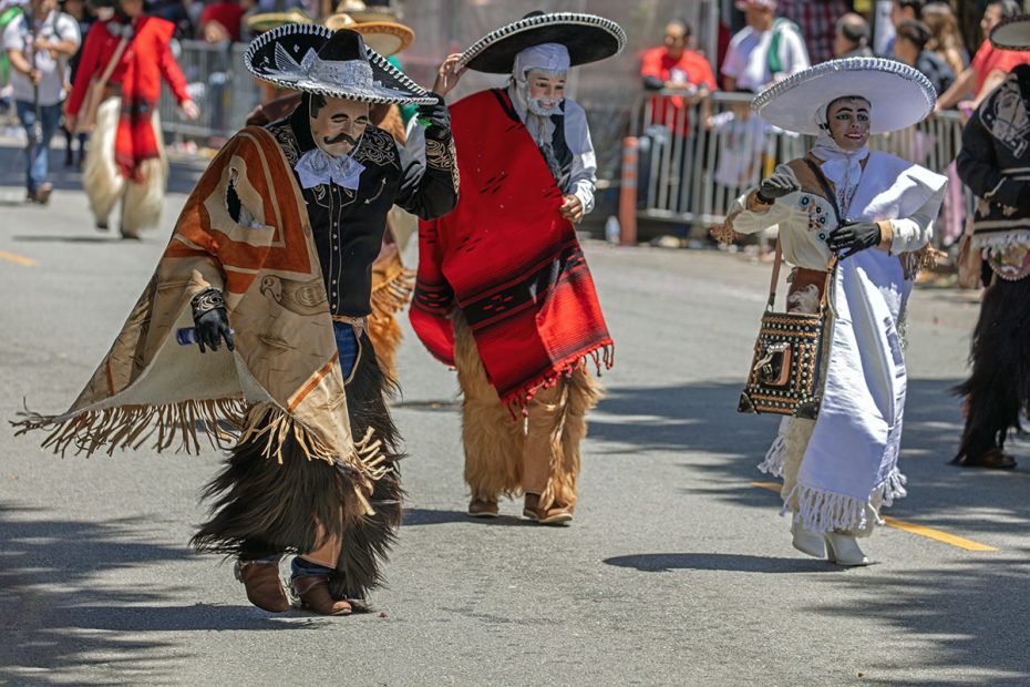 People dressed in traditional costumes and masks participate in a street parade.