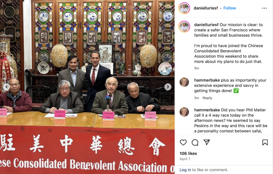 A group of five men, three seated and two standing, during a formal event at the Chinese Consolidated Benevolent Association with a red banner in front and ornate decorations in the background.