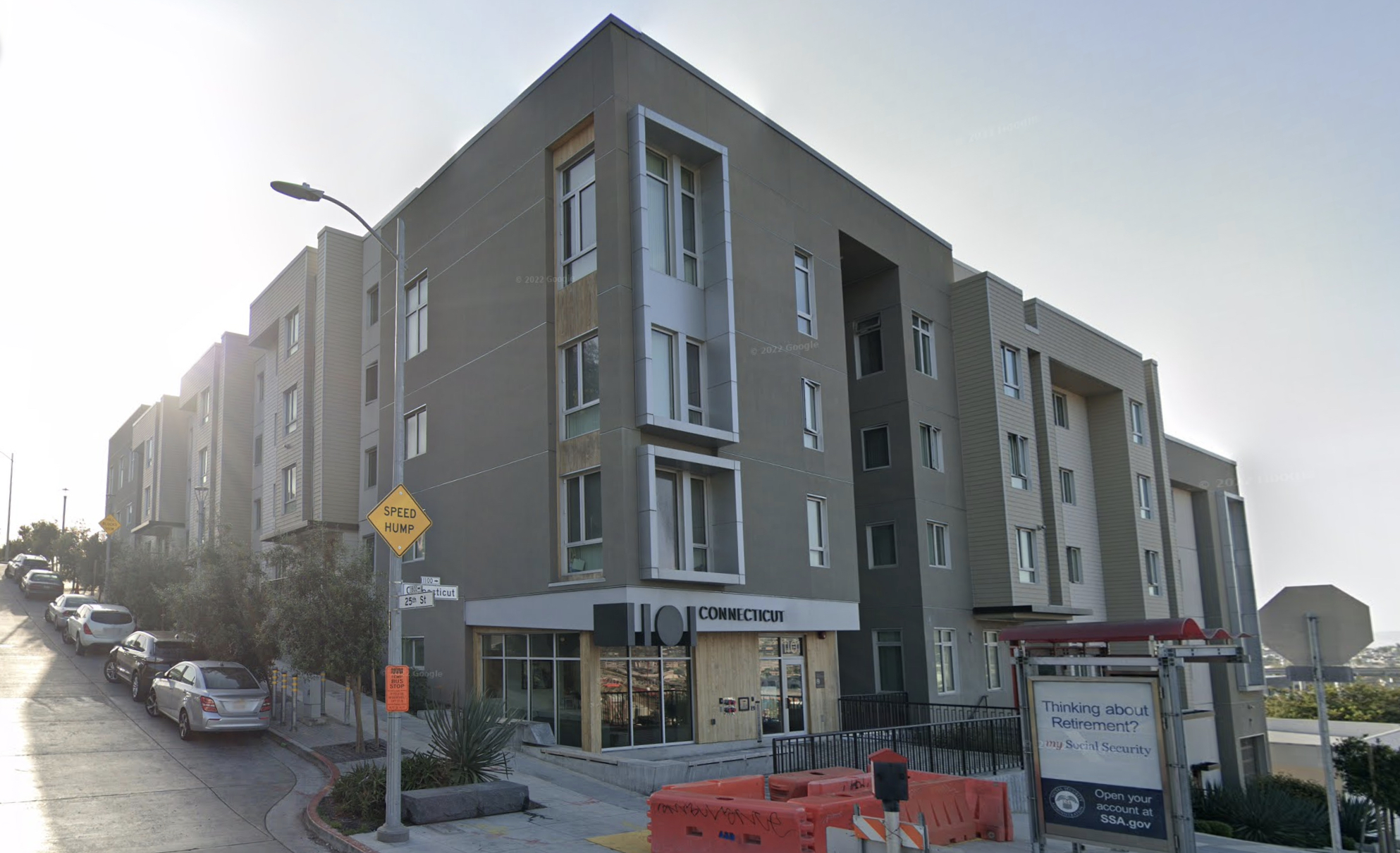 A modern multi-story apartment building with a store on the ground floor. Construction barriers and a street intersection are visible in the foreground.