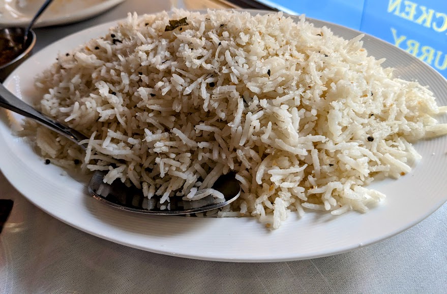 A plate filled with cooked white rice with a spoon placed on the side.