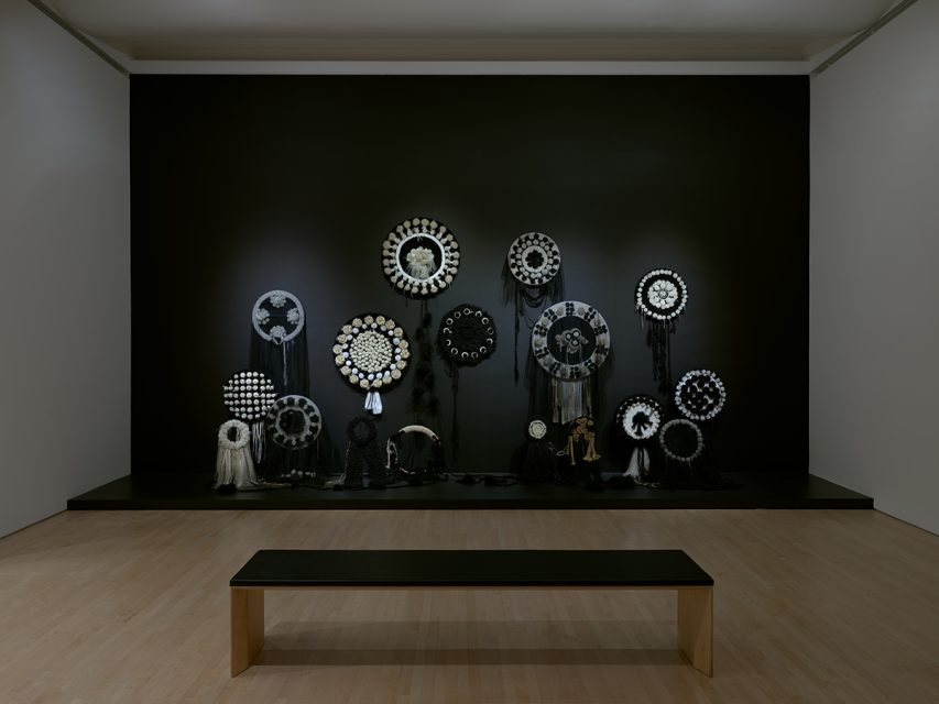Art installation featuring a dark wall with multiple circular, intricate black and white patterns, reminiscent of exhibits found in renowned museums, displayed in a gallery setting with a bench in the foreground.