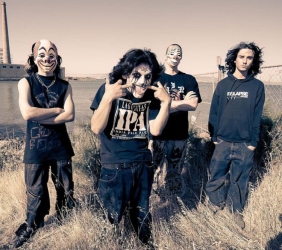 Four people wearing masks and casual clothing stand outdoors near water and industrial buildings.