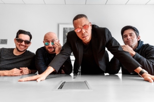Four men are posing confidently around a conference table, three of them wearing sunglasses.