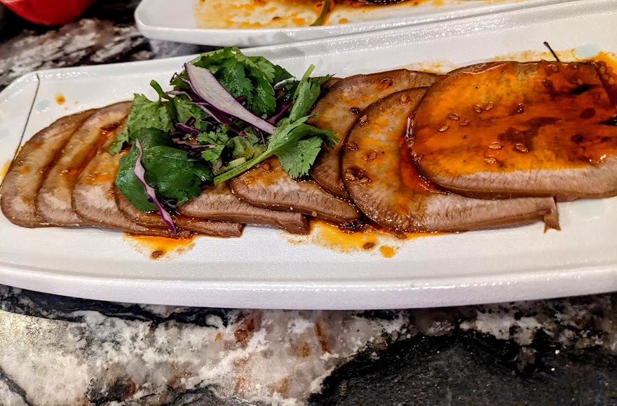 Slices of seared meat topped with green garnish and sauce on a white rectangular plate.