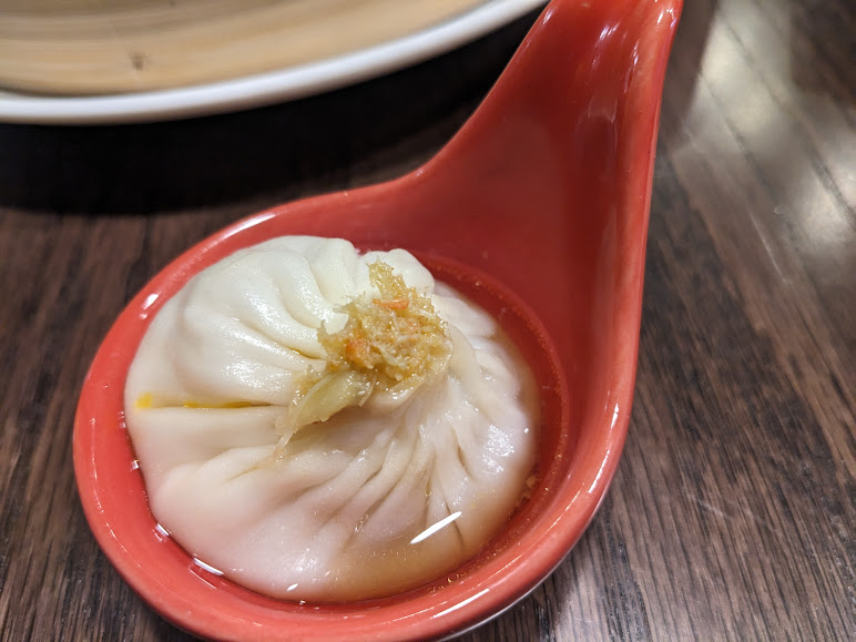 A soup dumpling in a red spoon, placed on a wooden table.