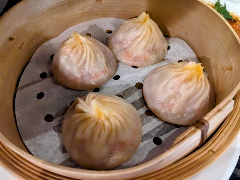 Four steamed dumplings in a bamboo steamer basket.