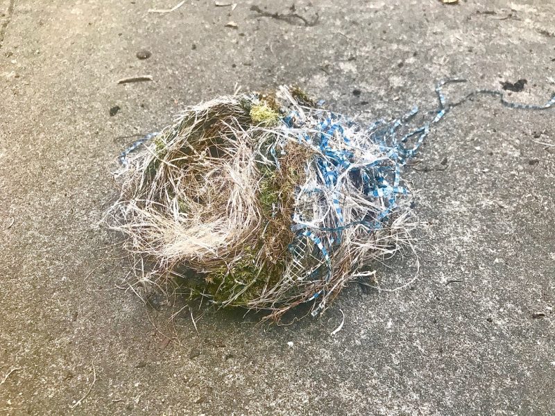 A bird's nest made from a mix of natural materials and synthetic fibers on a concrete surface.
