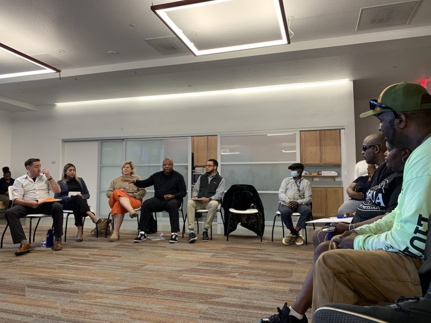A group of people sit in a circle having a discussion in a brightly lit room with modern decor.